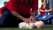 A person conducts first aid classes with a mannequin outdoors.