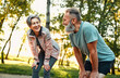 © HBS - Dynamic retirement. Emotional spouses taking few minutes for rest after fast running in forest. Mature husband and wife in activewear bending, keeping hands on knees, deeply breathing and laughing.