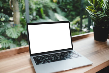 Wooden table with laptop white screen complemented by a vibrant potted plant blurred background. 