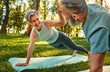 © HBS - Plank balance. Radiant grey-haired lady standing on plank with outstretched arm and giving high five to husband. Determined man and woman improving strength and endurance by joint workout on nature.