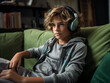 12jähriger blonder Junge sitzt auf einer grünen Couch im Wohnzimmer und hört Musik mit einem großen Kopfhörer