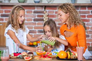 Mother and daughters cooking together in the kitchen. Healthy food concept. Portrait of happy family with fresh smoothies. Happy sisters.