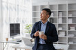 © amnaj - Happy smiling Asian businessman holding a coffee mug sitting happily in the office.