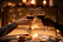 Close up of two people clinking wine glasses at dinner table with Christmas lights in background, copy space