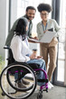 © LIGHTFIELD STUDIOS - happy interracial colleagues looking at disabled coworker on wheelchair, discussing work strategy