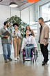 © LIGHTFIELD STUDIOS - diversity and inclusion, disabled woman in wheelchair looking at asian colleague near team