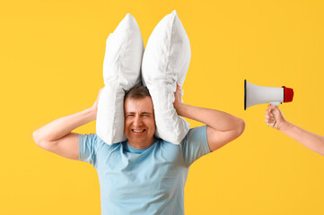 Wall Mural - Displeased mature man holding pillows and female hand with megaphone on yellow background