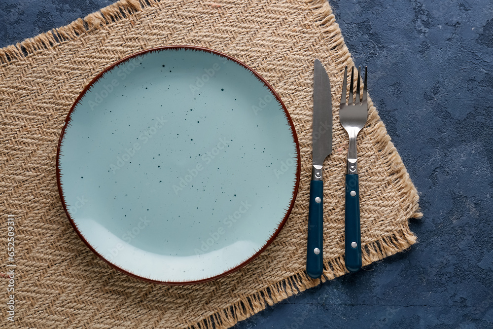 Silver knife with fork, plate and kitchen mat on blue grunge background