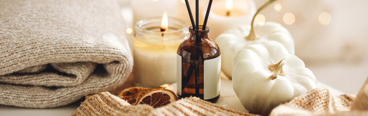 Autumn cozy mood composition on the windowsill. Aroma diffuser, pumpkins, dry citrus, candles on wooden tray, knitted warm plaid. Fall hygge home decor, aromatherapy. Copy space, banner white