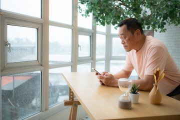 asian senior man using the smartphone to greet friends via text message in the balcony area of the h