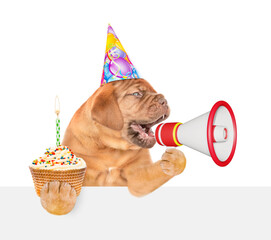 Poster - Funny Mastiff puppy wearing party cap barks into megaphone above empty white banner and holds cupcake with burning candle. isolated on white background