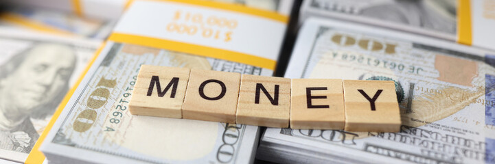 Wall Mural - Word money collected from wooden bars on stacks of dollars close-up.