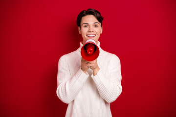 Poster - Photo of activist young positive student guy wear knitted white sweater hold megaphone protest winter holidays isolated on red color background