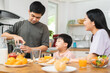 © KMPZZZ - Happy refreshment family breakfast in morning, asian young parent father, mother and little cute boy, child having meal in kitchen eating together at home. Cheerful, enjoy cooking people.