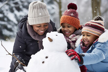 African Family Building Snowman At The Park In Winter