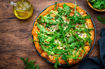 Wall Mural - Hot pizza with mozzarella cheese, ham, pesto sauce and fresh arugula, rustic wooden table background, top view