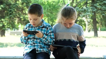 Wall Mural - Children use gadgets while sitting in the park outdoors, games on smartphone and tablet