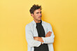 Young Latino man posing on yellow background suspicious, uncertain, examining you.