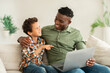 © Prostock-studio - Happy african father and son sitting with laptop at home