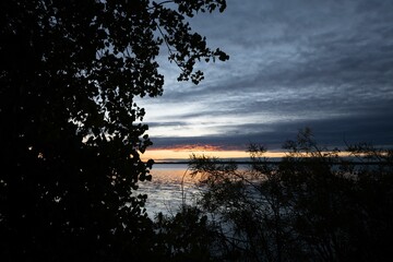 Wall Mural - Picturesque view of an orange sunrise over a lake seen through the trees