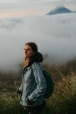Fototapeta  - Vertical shot of a female hiker in a denim jacket on a mountain over clouds