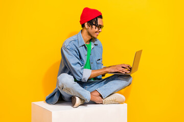 Sticker - Full body photo of attractive young man sitting white platform netbook typing wear trendy jeans clothes isolated on yellow color background