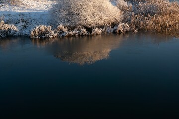 Wall Mural - Idyllic winter scene of a tranquil river covered in a layer of ice, illuminated by the setting sun