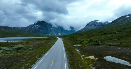 Wall Mural - landscape view showing a road with green hills and snowy mountains with misty sky in norway