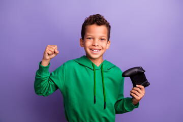 Poster - Photo of positive lucky little boy dressed green hoodie winning playstation game isolated purple color background