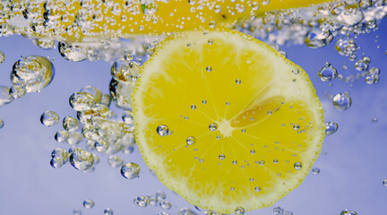 Wall Mural - Underwater of freshly squeezed sweetened lemonade which raw lemons slice falling in soda water against dark blue or black background. Close up lemonade or Highball lemon cocktail cold refreshing drink