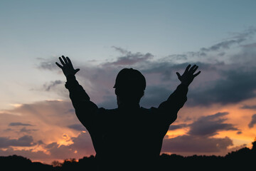 Wall Mural - A young Christian man with a beard in nature raises his hands to the sky, thanks God, praises.