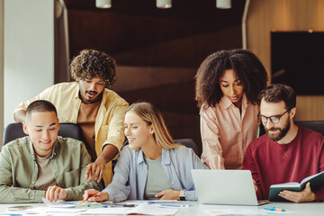 Wall Mural - Group of smiling multiracial university students using laptop studying  together, education concept. Young startup team, colleagues meeting, working, planning strategy in office. Successful business