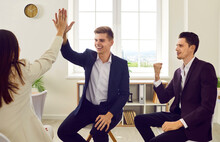 Group Of Young Three Business People Sitting In Office And Rejoicing At The Deal Is Struck. Man Giving High Five To A Woman Finishing Meeting Or Signing Contract Or Greeting New Employee.