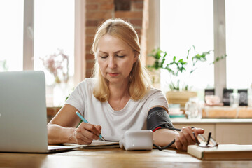 Senior woman measuring her blood pressure. Retired uses medicine digital device tonometer for control health at home