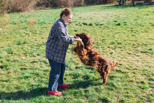 Human And A Dog. Woman And Her Friend Dog On The Field Background. Beautiful Irish Setter Dog Resting With Girl In Grass. Domestic Animals Concept