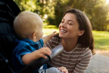 Young mother having fun with baby. The baby is sitting in the pram and having fun outdoors with her mom