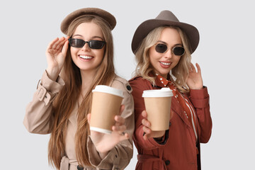 Wall Mural - Young sisters with cups of coffee on light background