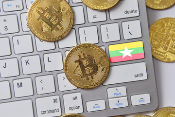 national flag of myanmar on the keyboard with bitcoin coins on a grey background.