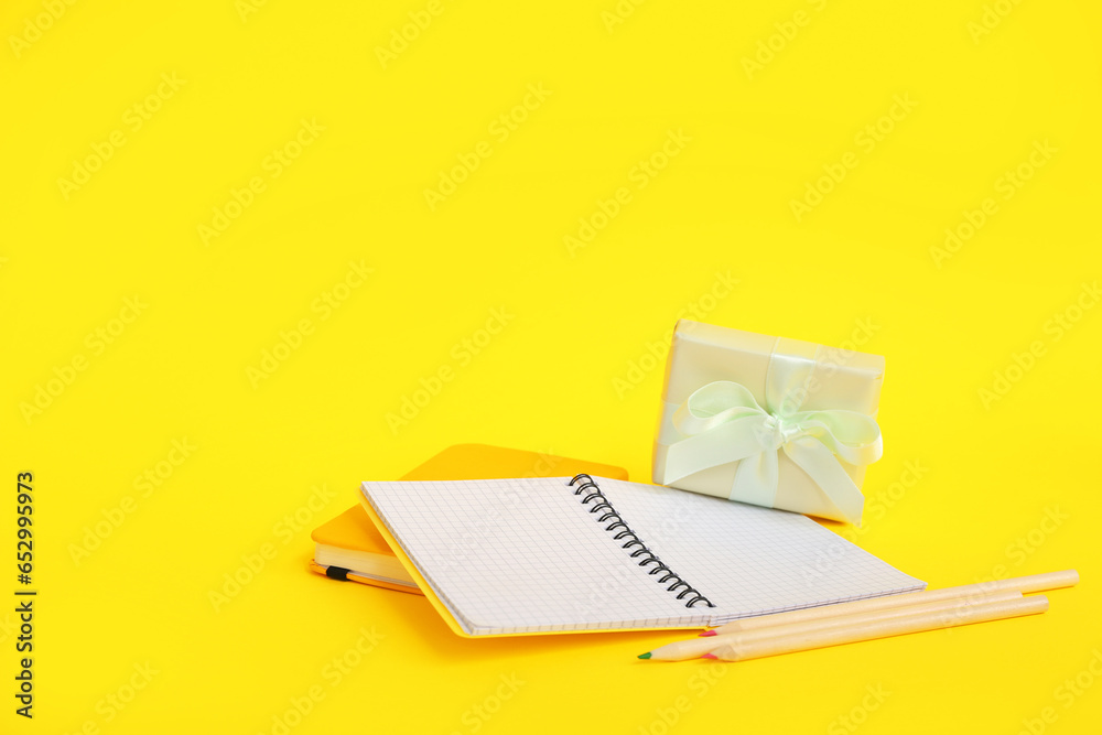 Gift box with notebooks and colorful pencils on yellow background
