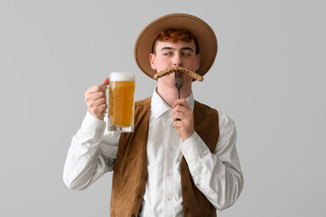 Young man in traditional German clothes with beer and sausage on light background