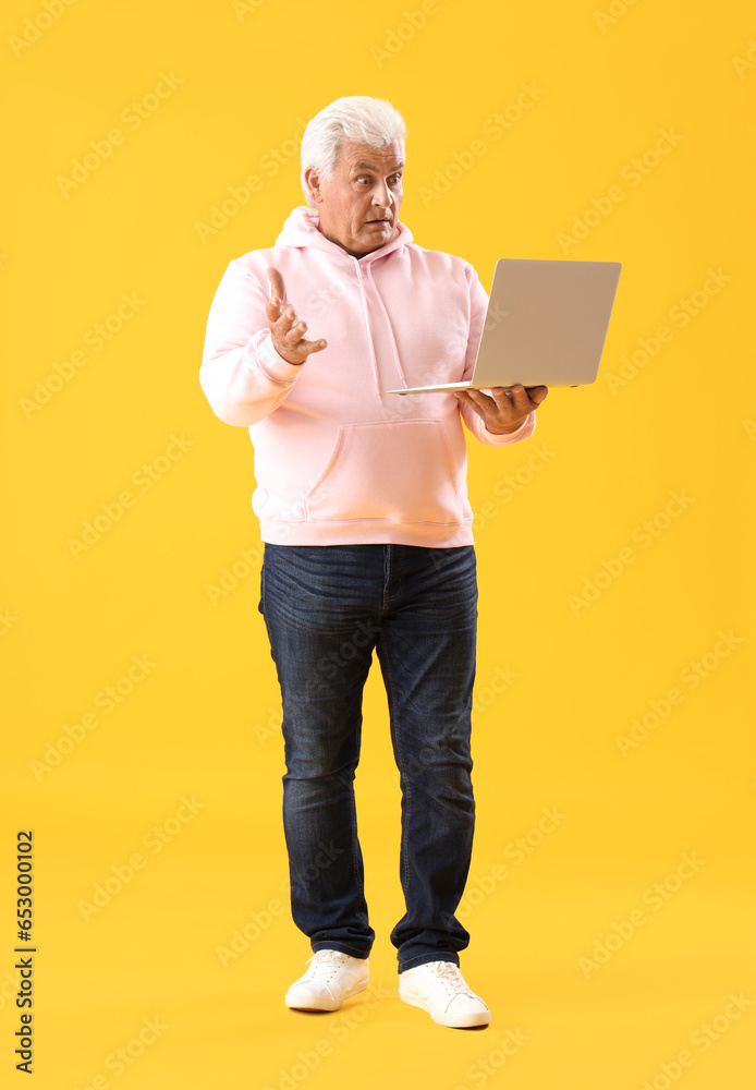 Shocked senior man using laptop on yellow background