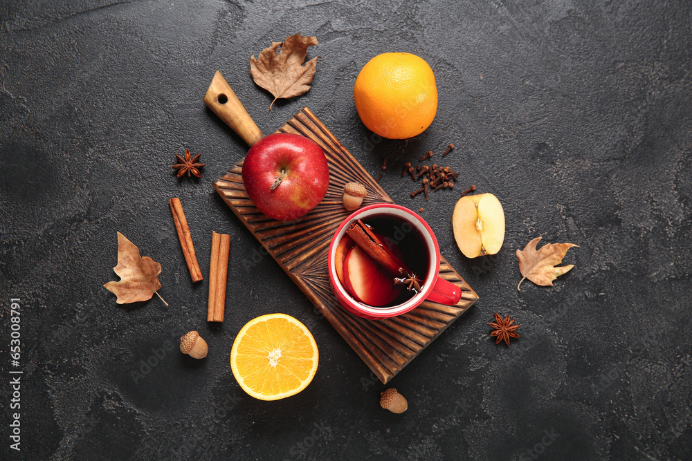 Cup of hot mulled wine with apple and orange on black background