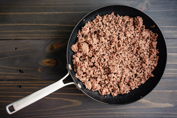 Wall Mural - Browned Ground Beef in a Large Skillet: Cooked ground beef in a large non-stick frying pan on a wooden table