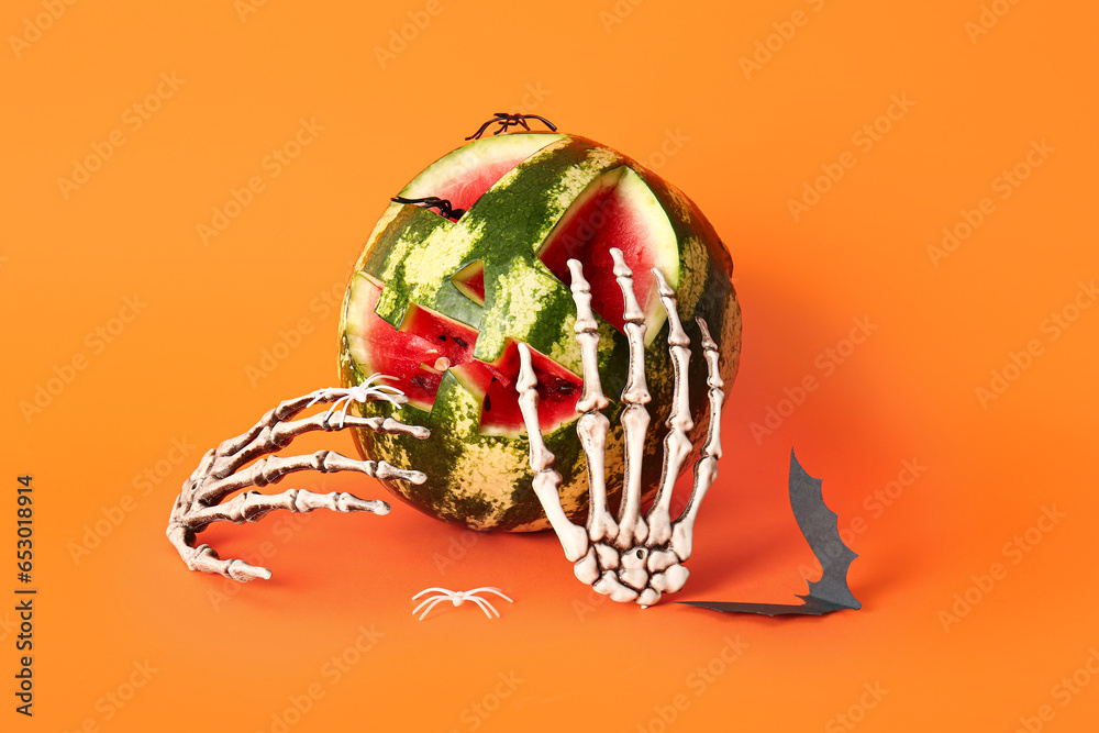 Carved watermelon for Halloween with skeleton hands, bat and spiders on orange background