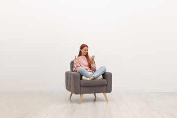 Sticker - Happy young woman having video chat via smartphone while sitting in armchair near white wall indoors