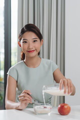 Wall Mural - Young woman pouring milk into bowl with breakfast