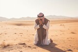 Fototapeta Kosmos - Muslim man praying, kneeling, in the Arabian desert.