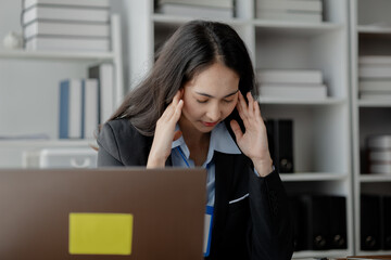 A woman sits in a company office and looks stressed. A businesswoman is stressed and tired from working hard. She works for a long time causing office syndrome. The concept of stress from work.