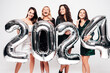 Four Beautiful women celebrating New Year. Happy gorgeous female in stylish sexy party dresses holding silver 2024 balloons, having fun at New Year's Eve Party. holiday celebration. Charming models