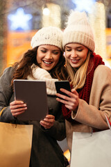 Wall Mural - Happy women friends using digital tablet for online shopping at Christmas in the city.